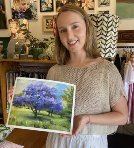 Artist Ellie Sweetman holding oil painting, Blooming Jacaranda